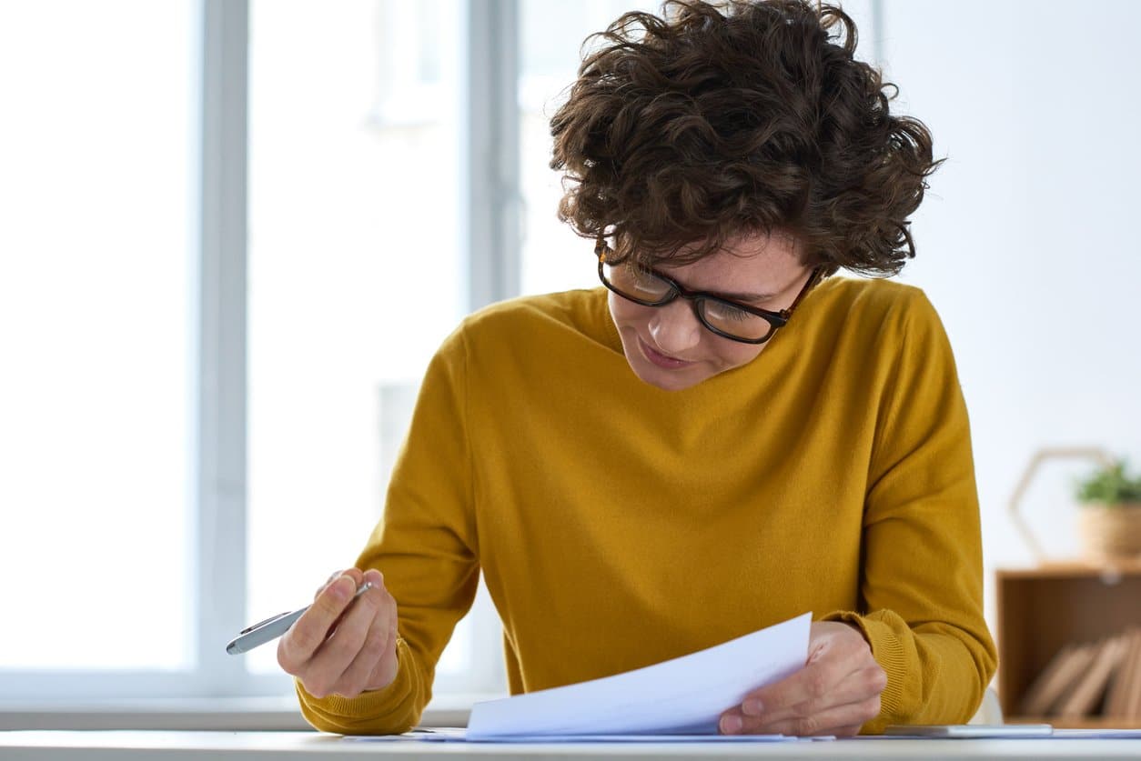 woman-sitting-at-desk-filling-out-paperwork-with-pen-and-windows-in-background