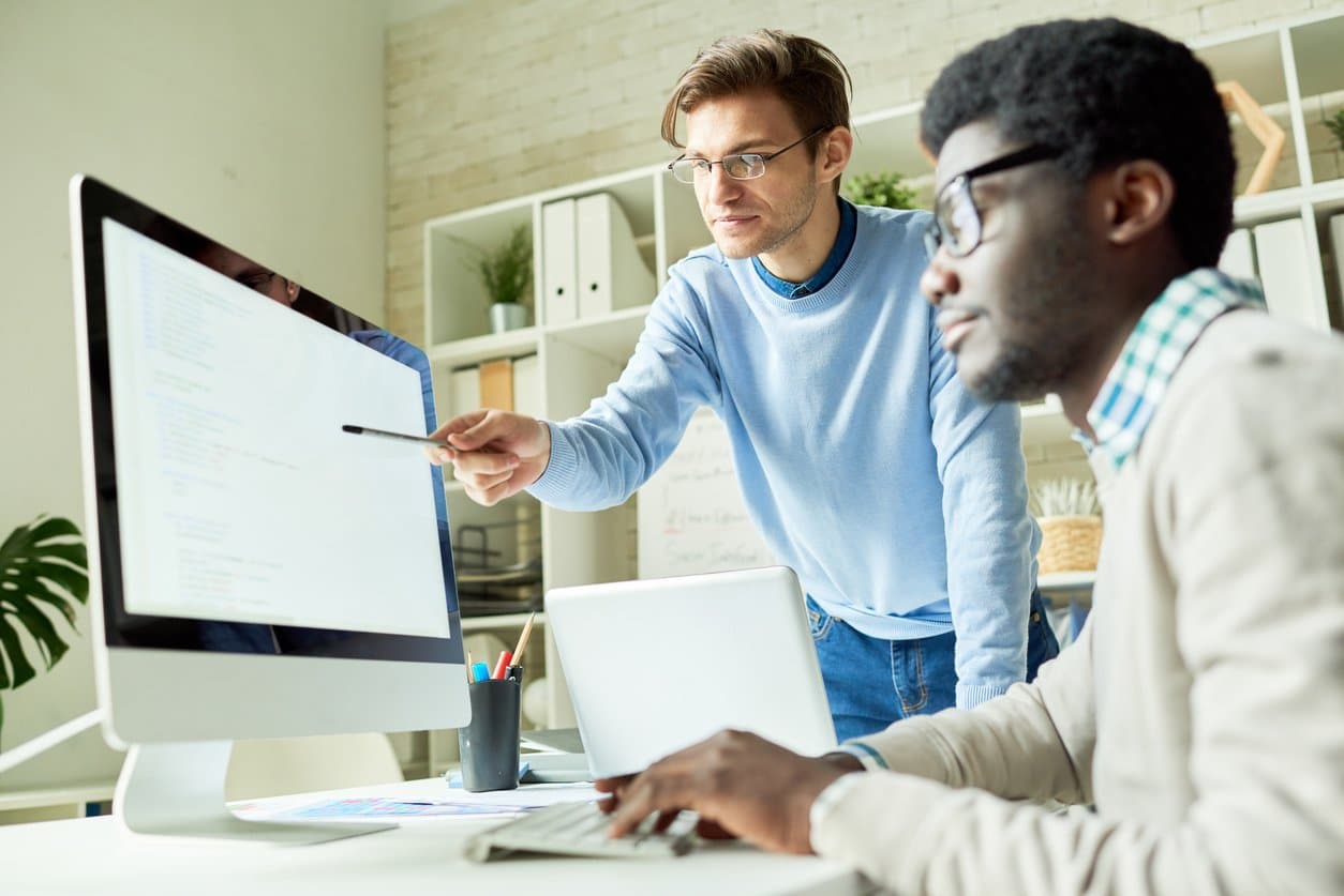 two-young-men-collaborating-at-work-in-front-of-bright-computer-monitor-on-desk