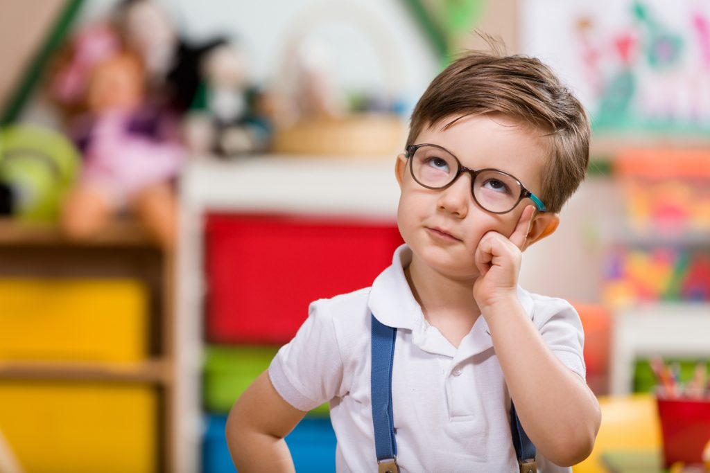 young boy wearing suspenders and glasses putting hand to face in thinking gesture