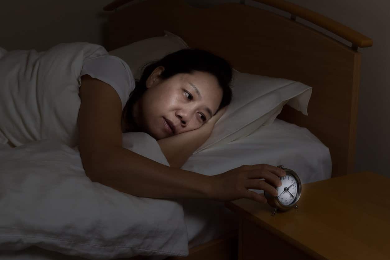woman in bed in dark room looking at illuminated alarm clock on side table