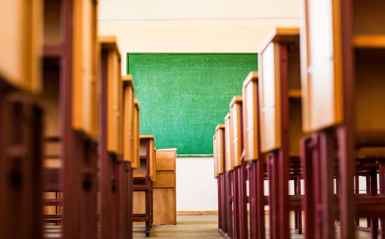 low angle view of classroom aisle with desks on either side and blackboard at front of room