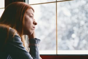 woman-suffering-from-seasonal-affective-disorder-looking-out-window-at-snowy-trees