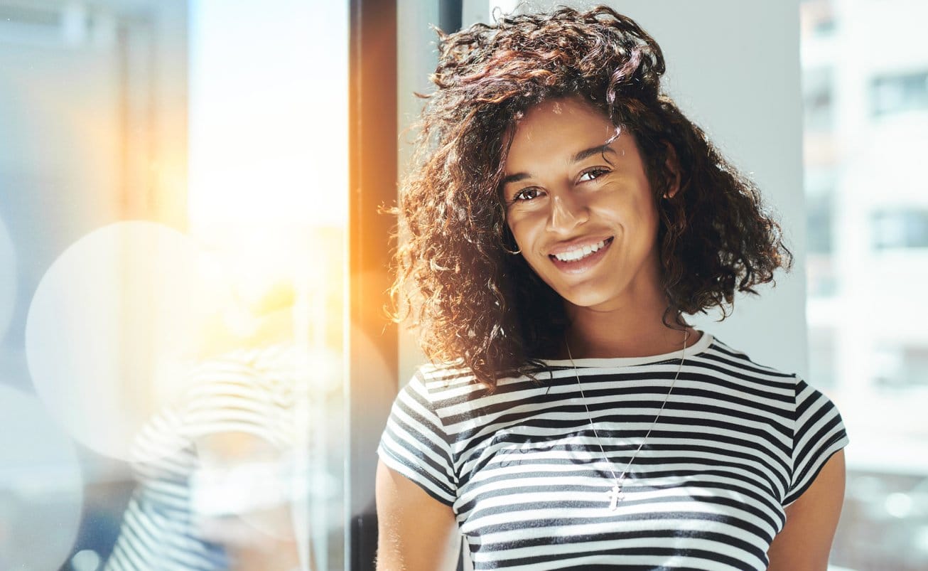 young-woman-in-striped-shirt-smiling-while-at-work-in-front-of-sunny-windows