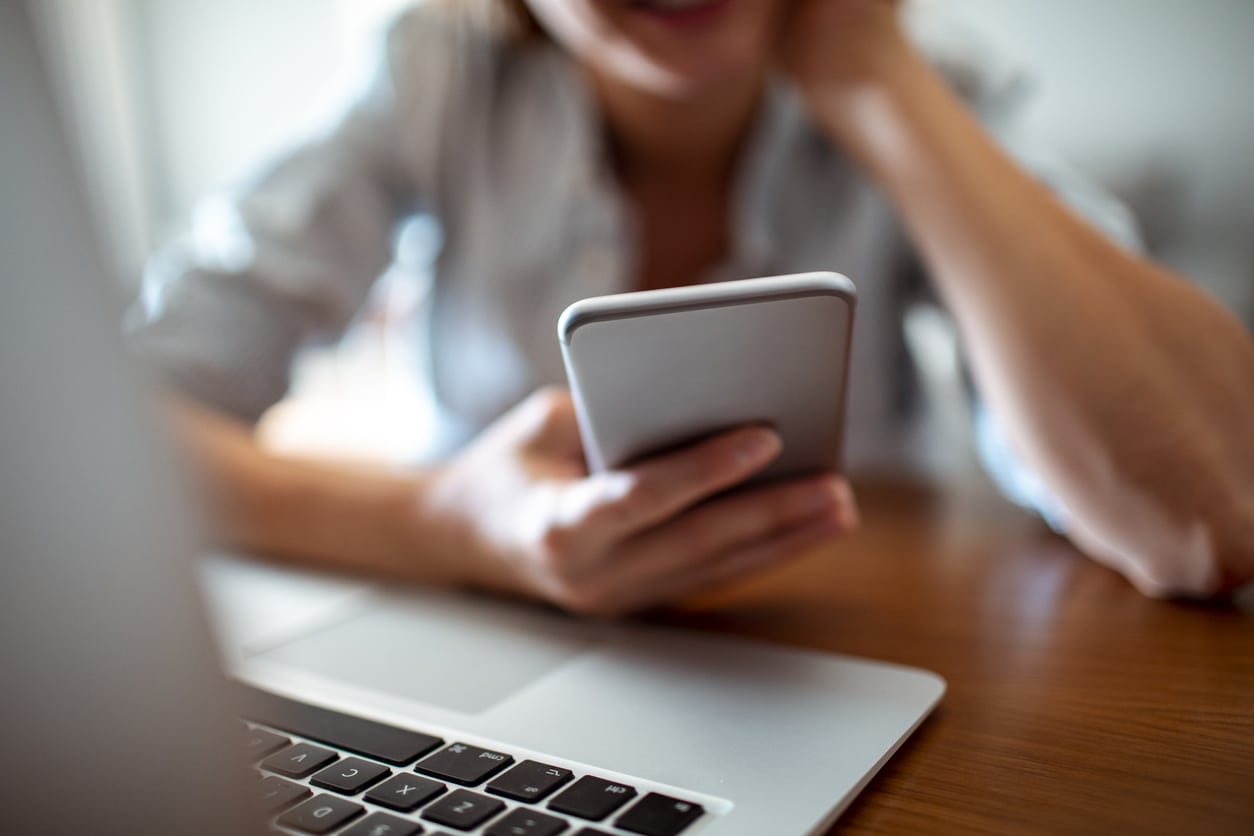 woman-at-desk-using-mobile-phone-and-laptop