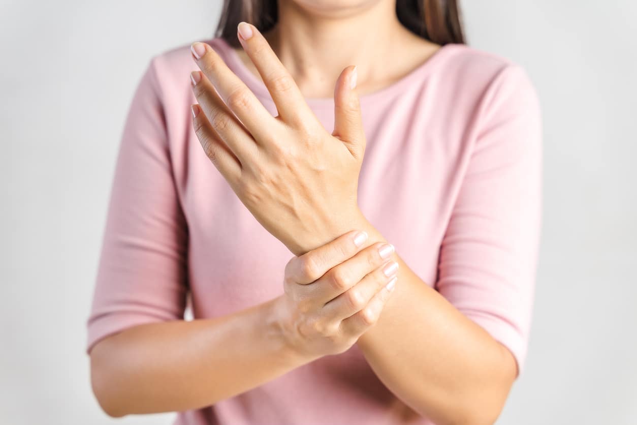 A woman holding her wrist to alleviate joint pain resulting from indoor lighting and lupus flare-ups.