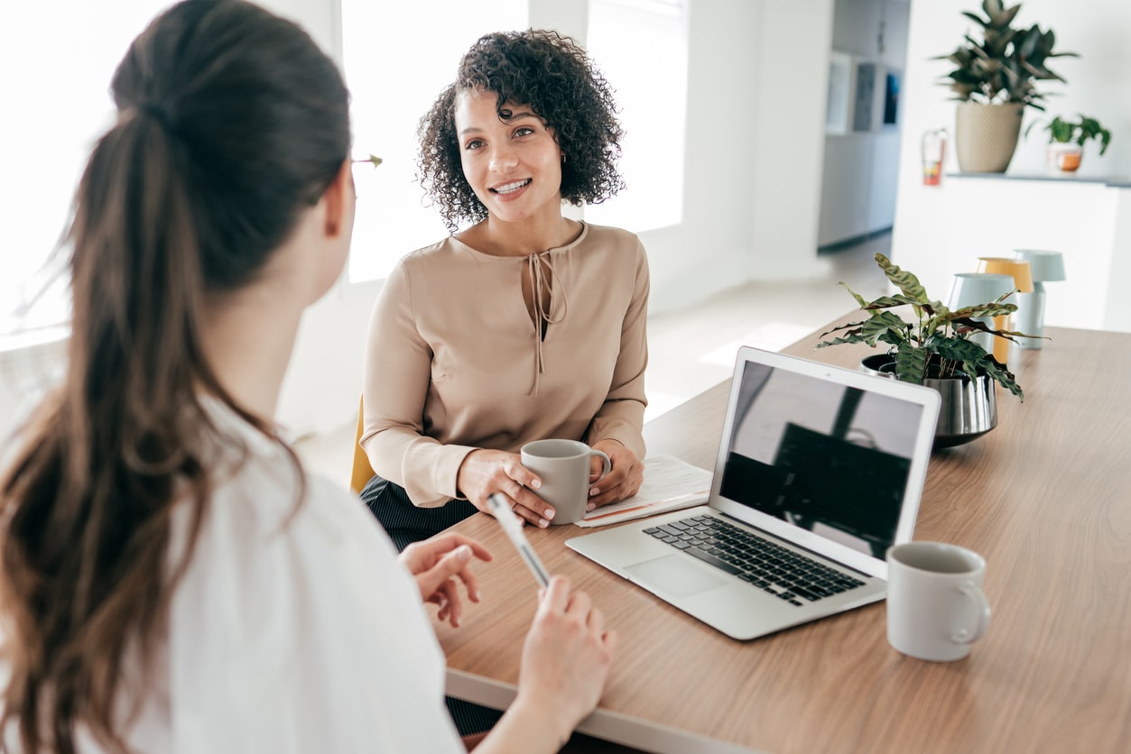 two-female-coworkers-sitting-at-table-with-laptop-near-bright-windows