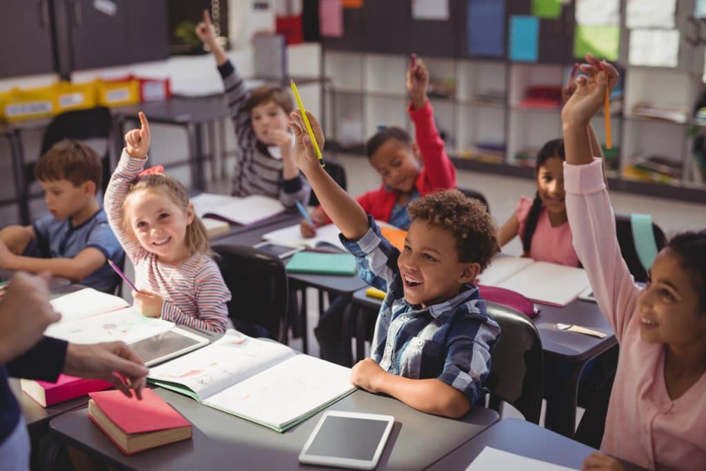children-at-desks-raising-their-hands-in-classroom