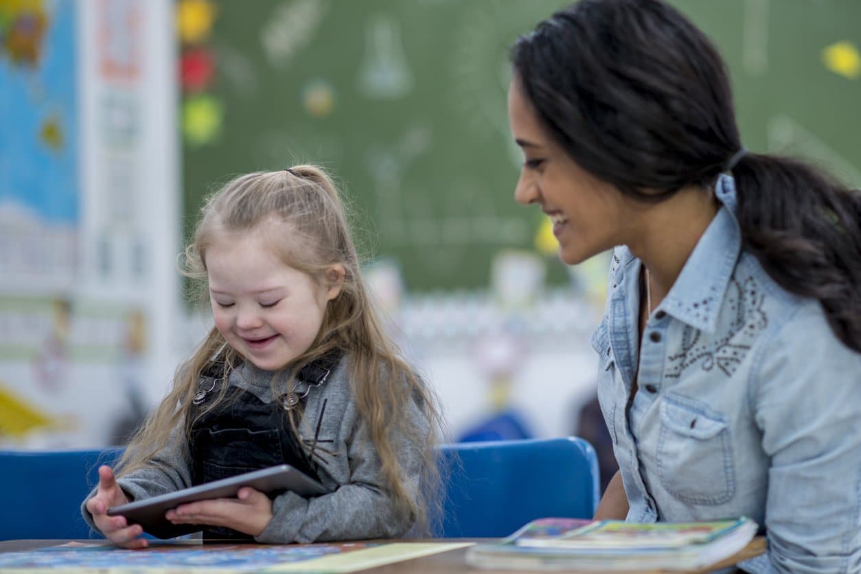 young-female-teacher-sitting-with-little-girl-with-down-syndrome-in-classroom