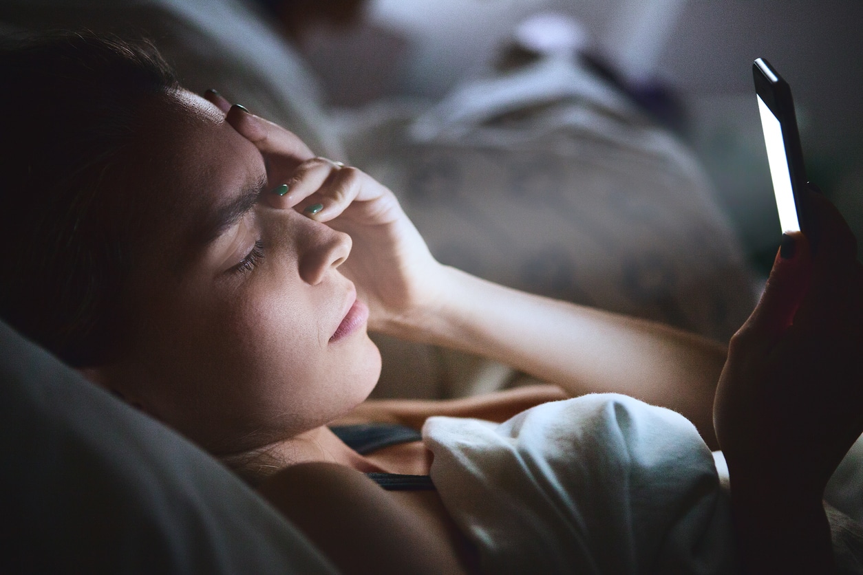 woman-holding-forehead-while-using-smartphone-in-bed-at-night