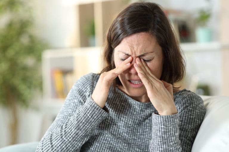 woman rubbing eyes due to sensitivity to sunlight