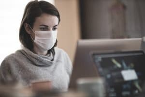 woman-wearing-surgical-mask-for-covid-19-while-sitting-at-table-and-working-on-laptop
