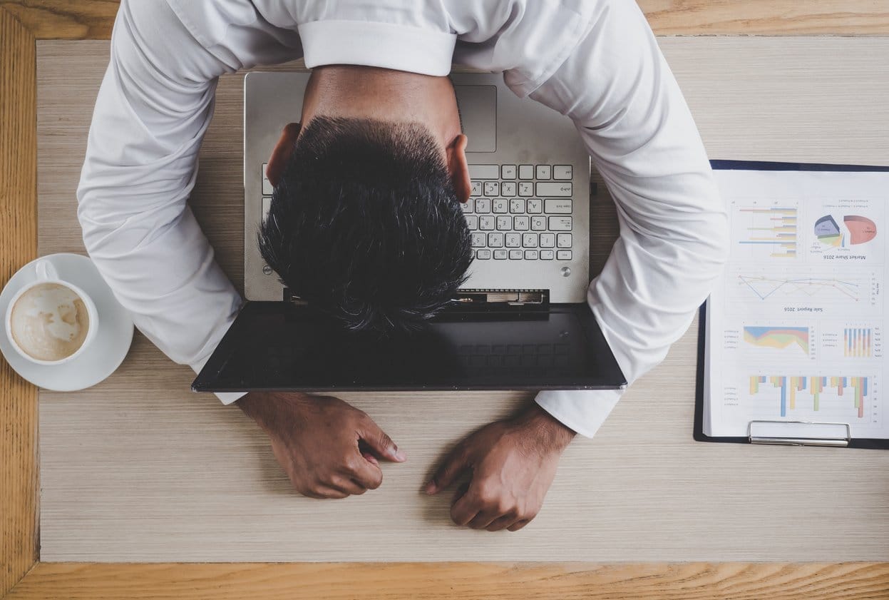 man-sitting-at-desk-with-head-down-on-open-laptop