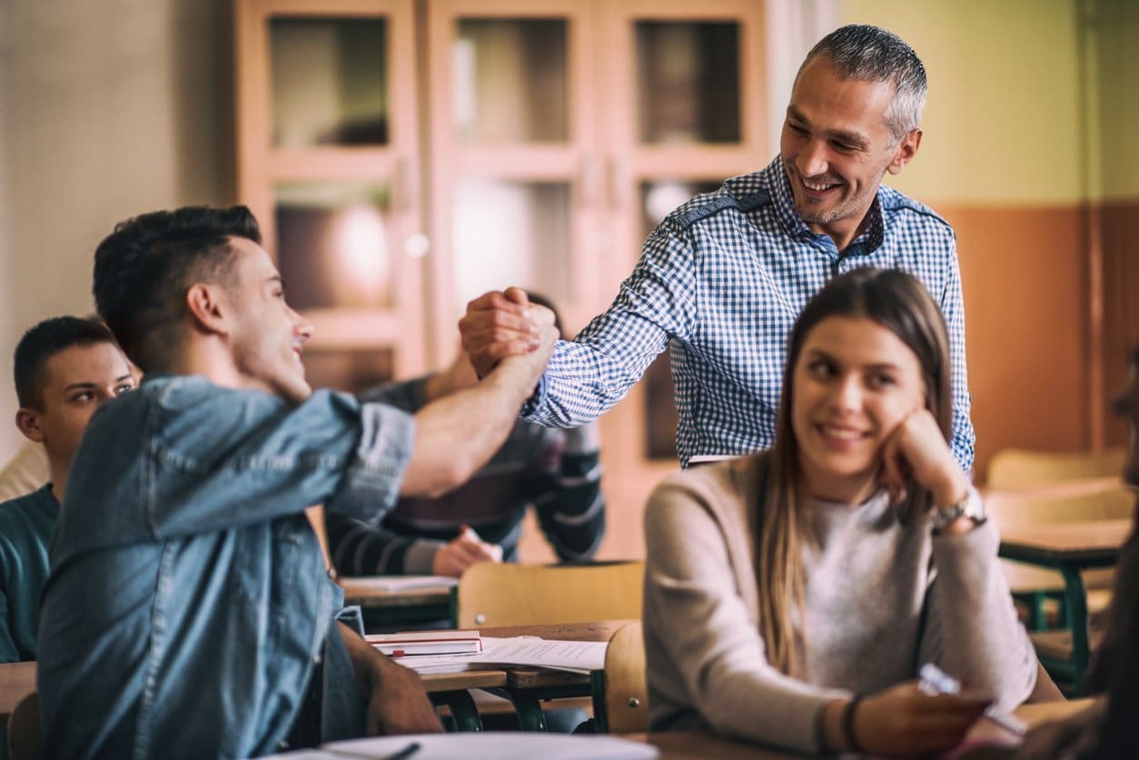 male-middle-age-teacher-giving-handshake-to-teenaged-student-in-classroom