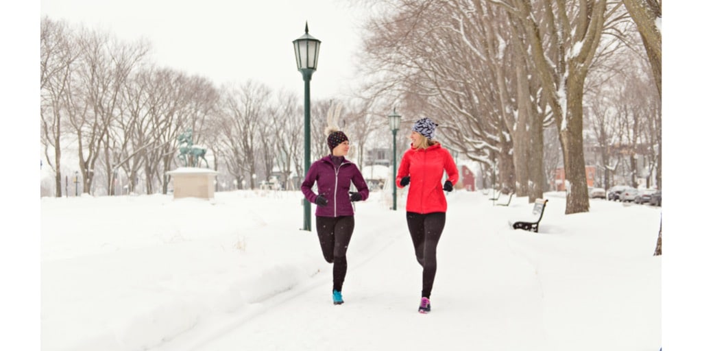 two-people-jogging-through-snowy-path-with-trees-and-streetlights
